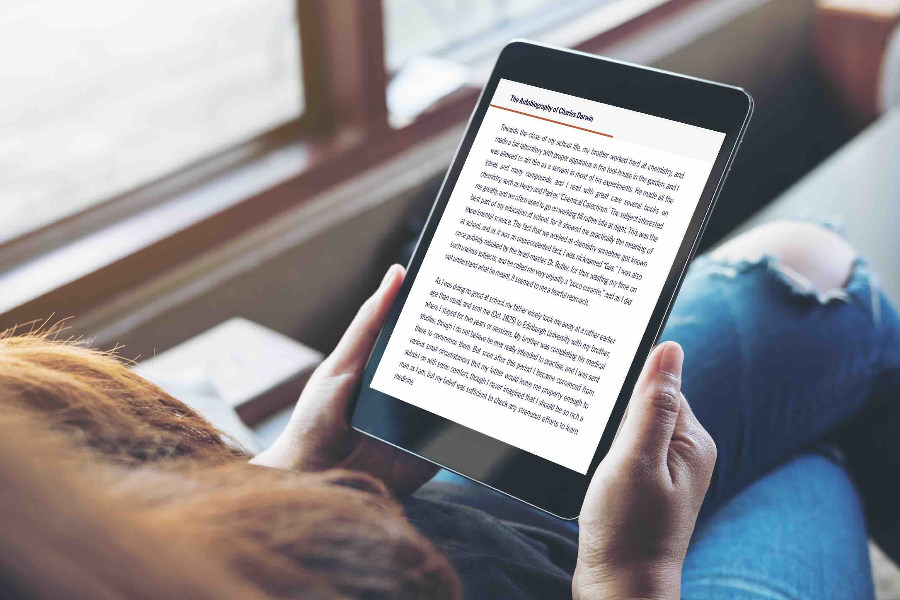 Person reads digital memoir story on tablet near window light.