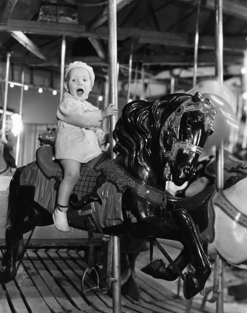 Smiling baby rides vintage carousel horse during childhood memory.