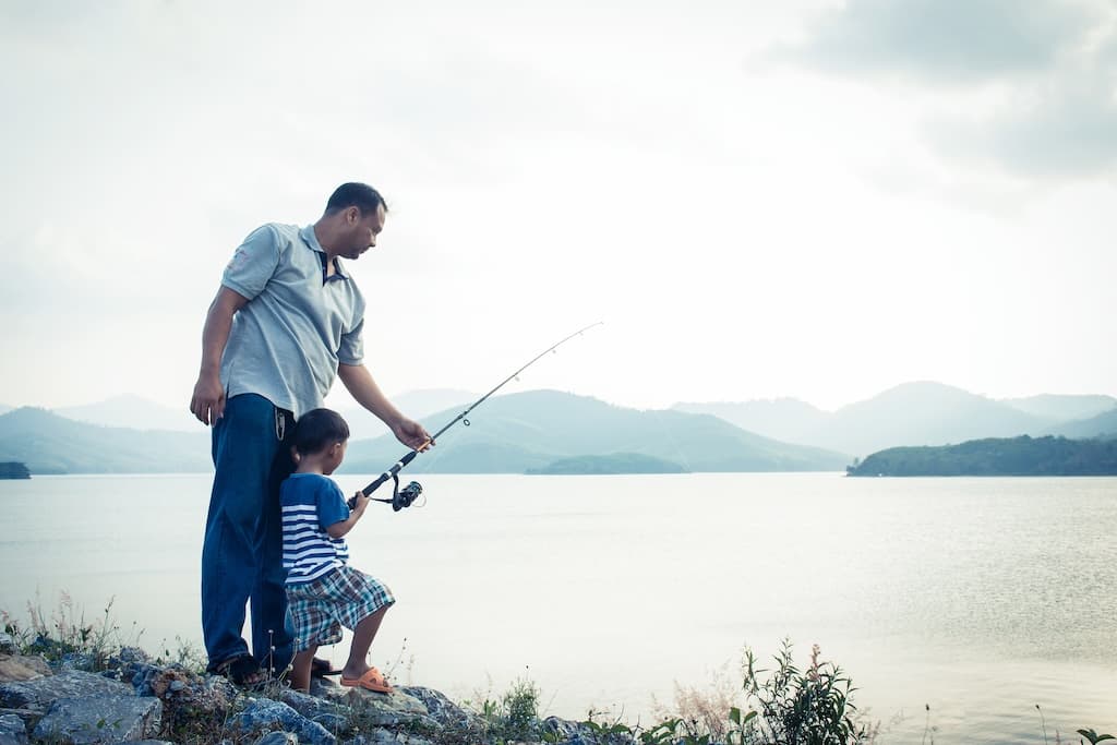 Father teaches young son to fish by peaceful mountain lake.