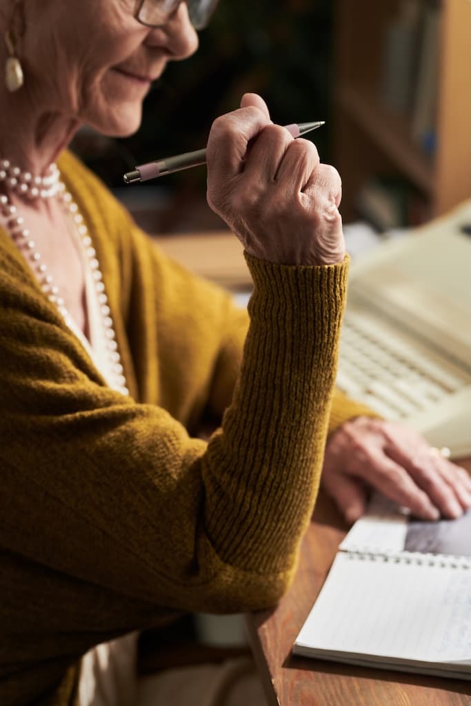 Older woman writes her life story thoughtfully at her desk.